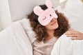 Young hispanic woman wearing sleepmask sleeping on bed at bedroom