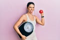 Young hispanic woman wearing sportswear holding weighing machine and apple sticking tongue out happy with funny expression Royalty Free Stock Photo