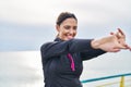 Young hispanic woman wearing sportswear stretching arms at seaside Royalty Free Stock Photo