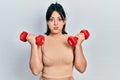 Young hispanic woman wearing sportswear using dumbbells puffing cheeks with funny face Royalty Free Stock Photo