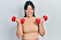 Young hispanic woman wearing sportswear using dumbbells sticking tongue out happy with funny expression Royalty Free Stock Photo