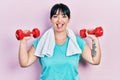 Young hispanic woman wearing sportswear using dumbbells sticking tongue out happy with funny expression Royalty Free Stock Photo