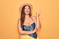 Young hispanic woman wearing summer hat and swimsuit over yellow background with a big smile on face, pointing with hand and Royalty Free Stock Photo