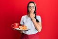 Young hispanic woman wearing waitress apron holding tray with breakfast covering mouth with hand, shocked and afraid for mistake Royalty Free Stock Photo