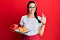 Young hispanic woman wearing waitress apron holding tray with breakfast doing ok sign with fingers, smiling friendly gesturing Royalty Free Stock Photo