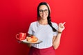 Young hispanic woman wearing waitress apron holding tray with breakfast smiling happy pointing with hand and finger to the side Royalty Free Stock Photo