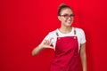 Young hispanic woman wearing waitress apron over red background smiling and confident gesturing with hand doing small size sign Royalty Free Stock Photo