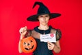 Young hispanic woman wearing witch costume holding pumpkin and happy halloween message depressed and worry for distress, crying