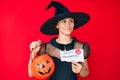 Young hispanic woman wearing witch costume holding pumpkin and happy halloween message smiling looking to the side and staring Royalty Free Stock Photo