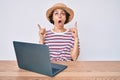 Young hispanic woman working with laptop sitting on the table amazed and surprised looking up and pointing with fingers and raised Royalty Free Stock Photo