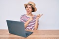 Young hispanic woman working with laptop sitting on the table smiling and looking at the camera pointing with two hands and Royalty Free Stock Photo