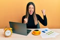 Young hispanic woman working at the office with laptop celebrating surprised and amazed for success with arms raised and eyes Royalty Free Stock Photo