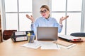 Young hispanic woman working at the office wearing glasses clueless and confused expression with arms and hands raised Royalty Free Stock Photo