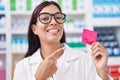 Young hispanic woman working at pharmacy holding condom smiling happy pointing with hand and finger Royalty Free Stock Photo