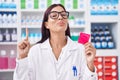 Young hispanic woman working at pharmacy holding condom smiling with an idea or question pointing finger with happy face, number
