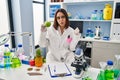 Young hispanic woman working at scientist laboratory holding fruit scared and amazed with open mouth for surprise, disbelief face Royalty Free Stock Photo