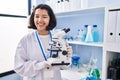 Young hispanic woman working at scientist laboratory holding microscope winking looking at the camera with sexy expression, Royalty Free Stock Photo