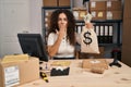 Young hispanic woman working at small business ecommerce holding money bag covering mouth with hand, shocked and afraid for Royalty Free Stock Photo