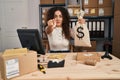 Young hispanic woman working at small business ecommerce holding money bag pointing with finger to the camera and to you, Royalty Free Stock Photo