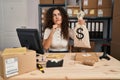 Young hispanic woman working at small business ecommerce holding money bag serious face thinking about question with hand on chin, Royalty Free Stock Photo