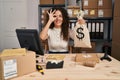 Young hispanic woman working at small business ecommerce holding money bag smiling happy doing ok sign with hand on eye looking Royalty Free Stock Photo