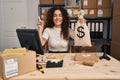 Young hispanic woman working at small business ecommerce holding money bag smiling happy pointing with hand and finger to the side Royalty Free Stock Photo