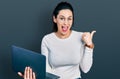 Young hispanic woman working using computer laptop pointing thumb up to the side smiling happy with open mouth Royalty Free Stock Photo