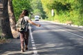 Young hitchhiker with backpack behind her back stops an approaching van with her thumb raised