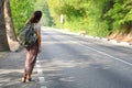 Young hitchhiker with backpack behind her, stands at the edge of the track and peers into the distance Royalty Free Stock Photo