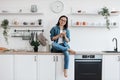 Young homebody resting with mobile on countertop in kitchen