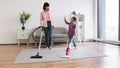 Young homemakers utilizing vacuum cleaners in living room