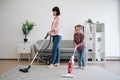 Young homemakers utilizing vacuum cleaners in living room