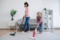 Young homemakers utilizing vacuum cleaners in living room