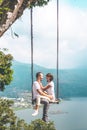 Young honeymoon couple swings in the jungle near the lake, Bali island, Indonesia.