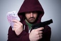 Young hooded man holding cash and gun in his hands Royalty Free Stock Photo