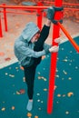 Young hooded martial artist woman warming up at playground pillars and doing splits