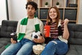 Young hooligan couple supporting soccer team sitting on the sofa at home