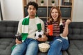 Young hooligan couple supporting soccer team sitting on the sofa at home