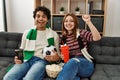 Young hooligan couple supporting soccer team sitting on the sofa at home