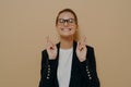 Young hopeful female student in eyeglasses crossing her fingers with hope and asking for good luck before exam