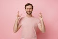 Young hopeful man squeezing his eyes and holding fingers crossed isolated