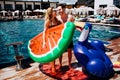 Young hot couple resting at swimpool. Woman and man look at each other. Holding colorful swimming rings. Stand at edge