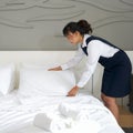 Young hotel maid making the bed. Hotel staff in blue uniform preparing room for guest