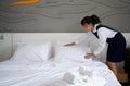 Young hotel maid making the bed. Hotel staff in blue uniform preparing room for guest