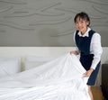 Young hotel maid with a smile making the bed. Staff in blue uniform preparing room for hotel guest