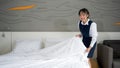 Young hotel maid with a smile making the bed. Staff in blue uniform preparing room for hotel guest