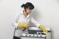 Young housemaid cleaning stove against gray background