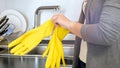 Young housewife protecting hands with yellow rubber gloves before doing house work