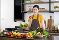 Young housewife with a smile holding red bell pepper. The kitchen counter full of various kinds of vegetables