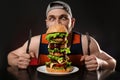 Young hungry man with cutlery eating huge burger on black